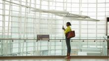 Passenger in yellow jacket and large over-the-shoulder bag at SEA Airport's Gina Marie Lindsay Hall checks her phone