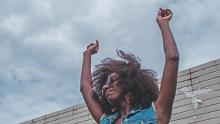 Woman dancing alone with hands in the air and blue sky above