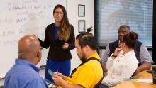 Mixed group of employees in a meeting with woman at a whiteboard leading the meeting.