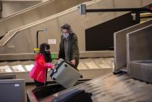 A child picking up her luggage with her parent