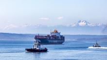 Hapag Lloyd container vessel in Elliott Bay guided by two tugs with snowy Olympic Mountains in the distance