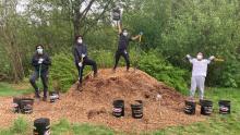 Four young men participants pose with shovels on and next to a pile of woodchips summer 2021