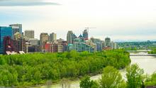 Peace Bridge in Calgary Alberta spans the river in the distance with green lush shoreline and skyline of the city 