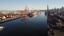 View of the East Waterway looking north. The image shows the channel with a container terminal on each side that has shipping containers, cranes, and container ships docked.
