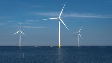 3 enormous offshore wind turbines against a clear sky above the horizon of dark blue water