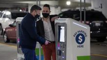 Two tall men wearing face coverings and blazers pay at an automated kiosk at SEA garage Dec 2022