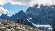 Three backpackers stand high atop a mountain in the Cascade Mountains in the North Cascades National Park with high peaks hidden in clouds