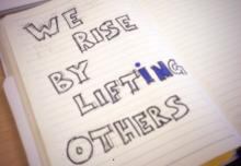 We Rise by Lifting Others image written on a notebook
