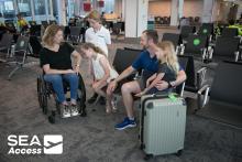 Family waits in the gate area with a suitcase. One parent is in a wheelchair.