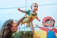 Infant is held up by parent and holds out their arms like they are flying.